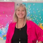Kate Taylor standing in front of two of her brilliantly coloured abstract paintings